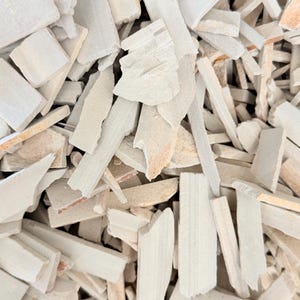 May include: A collection of small, irregular, flat fragments of off-white and light beige stone. The pieces vary in shape and size, featuring rough, matte textures and sharp, jagged edges layered densely across the entire frame.