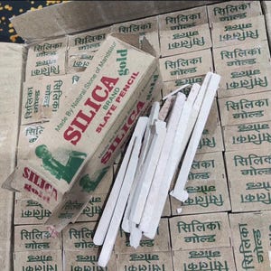 Könnte beinhalten: Schieferstifte und Schachteln. Auf den Schachteln steht "SILICA GOLD BRAND SLATE PENCIL" und "Made By Natural Stone of Mandsaur". Die Stifte sind weiß und rechteckig. Die Schachteln sind braun mit grünem und rotem Text.