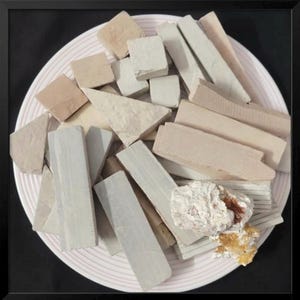 Könnte beinhalten: Eine Ansammlung verschieden geformter Tonstücke in hellen Farbtönen wie Beige, Grau und Braun, angeordnet auf einem Teller mit rosa Rand. Die Stücke umfassen Rechtecke, Quadrate und Dreiecke, sowie einige raue Felsformationen.