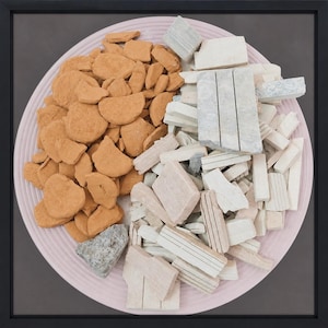 Peut inclure: Une œuvre d'art encadrée représentant une assiette rose avec un bord texturé. L'assiette est divisée en sections, l'une remplie de morceaux orange de forme irrégulière et l'autre de fragments de pierre blancs et gris de différentes tailles.