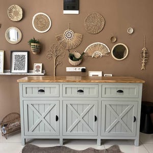 May include: A grey cabinet with a light wood top and black handles. The cabinet doors feature an X-shaped design. Woven wall decor and framed art hang on the brown wall above the cabinet. A decorative rug is on the floor.
