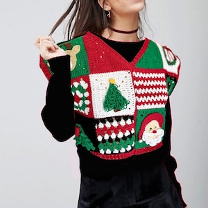 Könnte beinhalten: Eine farbenfrohe, gehäkelte Weihnachtsweste mit Patchwork-Design. Die Weste zeigt festliche Quadrate mit Rentieren, Weihnachtsbäumen, dem Weihnachtsmann und anderen festlichen Mustern in Rot, Grün, Weiß und Gold. Sie wird über einem schwarzen Langarmshirt und mit einem schwarzen Rock getragen.