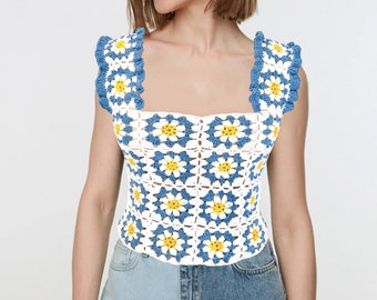 May include: White crochet top with blue and yellow daisy flowers. The top has a square neckline and sleeveless design.