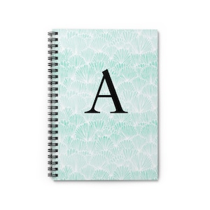 Puede incluir: Un cuaderno de espiral con un diseño en forma de abanico en color turquesa y blanco. Una gran letra "A" negra está centrada en la portada. El cuaderno está diseñado para escribir y tomar notas.