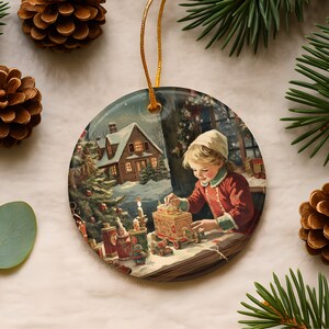 May include: A round ceramic Christmas ornament featuring a nostalgic illustration of a child in a red coat playing with a toy train. The scene includes a snow-covered cabin, a decorated tree, and warm candlelight, all suspended by a gold cord.