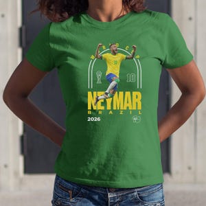 A green t-shirt with a graphic design featuring a soccer player in a yellow jersey, celebrating with raised arms.