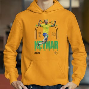 A yellow hoodie with a graphic of a soccer player in mid-jump, celebrating, and the text "NEYMAR BRASIL" and "2026" printed on it.