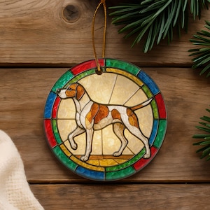 May include: A circular hanging ornament featuring a stained-glass style illustration of a white and brown pointer dog. The dog is centered within a border of alternating red, green, and blue glass-like segments, suspended by a thin gold cord.
