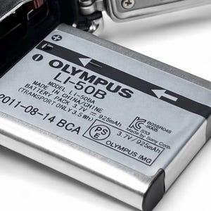 May include: A silver Olympus LI-50B camera battery, with black text indicating the model, voltage, and manufacturing details. The battery is partially inserted into a camera, with a metallic gray finish.