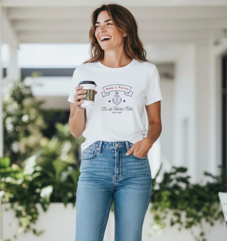 Pode incluir: Camiseta branca com o texto "Rare & Rising" acima de um gr&aacute;fico de &acirc;ncora e "For the Global Elite" abaixo. A camiseta &eacute; combinada com jeans azuis. Uma pessoa est&aacute; segurando uma x&iacute;cara de caf&eacute;.