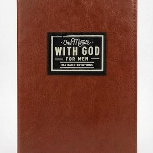 May include: A brown leather-bound book with the title "One Minute With God For Men" in a black and white rectangular label. The book cover is a solid, warm brown color, and the text indicates 365 daily devotions.
