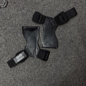 Puede incluir: Agarres de halterofilia negros con correas de mu&ntilde;eca ajustables. Los agarres est&aacute;n hechos de un material texturizado y presentan el texto "Lifting Infinite" en una de las correas. Dise&ntilde;ados para proteger las manos.