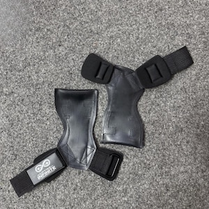 May include: Two black weightlifting grips with wrist straps. The grips are made of leather-like material and have a padded area for the palm. The wrist straps have a metal buckle and a label that reads "Lifting Infinite".
