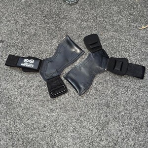 Puede incluir: Par de agarres de halterofilia negros con correas de mu&ntilde;eca ajustables. Los agarres est&aacute;n hechos de un material texturizado y presentan el texto "Lifting Infinite" con un s&iacute;mbolo de infinito.