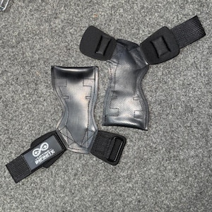 May include: Pair of black weightlifting grips with wrist straps. The grips are made of a durable material and feature a contoured design for a secure fit. The wrist straps have the text "Lifting Infinite" and an infinity symbol.