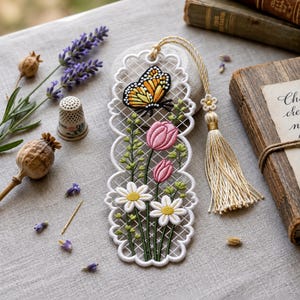 May include: A white lace bookmark featuring embroidered pink tulips, white daisies, and a monarch butterfly. The bookmark has a scalloped edge and a long, cream-coloured tassel attached to the top with a small flower-shaped bead detail.