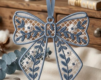 May include: A decorative bow ornament featuring intricate blue and white embroidery on a lattice-style mesh base. The design includes embroidered blue leaves and small white flowers with blue centers, suspended by a matching blue satin ribbon loop.