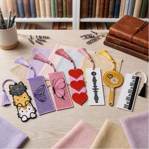 May include: A collection of seven embroidered bookmarks with tassels, featuring designs of three stacked cats, a purple butterfly on a honeycomb pattern, a pink butterfly, three red hearts, a sound wave, a yellow daisy with a bee, and piano keys.