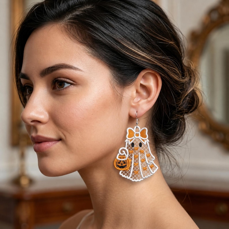 May include: A white ghost-shaped earring featuring an orange bow at the top and an orange jack-o'-lantern bucket held by the ghost. The ghost design has a delicate white lattice pattern with small orange star accents and two black oval eyes.