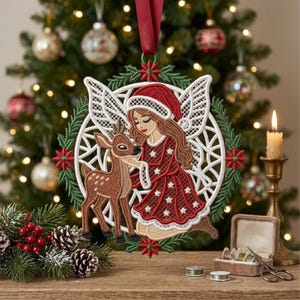 Puede incluir: Un adorno navideño bordado circular que muestra una figura de cabello castaño largo con gorro de Papá Noel y vestido rojo con estrellas blancas, arrodillada junto a un cervatillo marrón, enmarcado por un borde de encaje blanco y acebo.