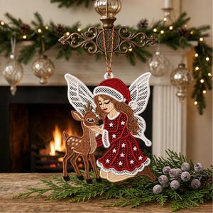 May include: A hanging Christmas ornament featuring an embroidered design of a fairy with long brown hair wearing a red Santa hat and a red dress with white stars, kneeling beside a brown fawn. The fairy has white lace-like wings.