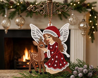 May include: A hanging Christmas ornament featuring an embroidered design of a fairy with long brown hair wearing a red Santa hat and a red dress with white stars, kneeling beside a brown fawn. The fairy has white lace-like wings.