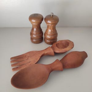 Op de afbeelding: Een houten keukenset met twee bruine zout- en pepermolens, een saladevork en twee saladelepels. De items zijn gemaakt van hout en hebben een natuurlijke afwerking. De set is ontworpen voor het serveren van salades en het kruiden van voedsel.