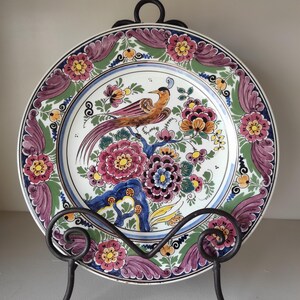 Puede incluir: Plato decorativo de cerámica con un diseño de pájaro y flores. El plato tiene un fondo blanco con un diseño floral colorido en tonos de rosa, naranja, azul y verde. El plato se exhibe en un soporte de metal negro. Diámetro: aproximadamente 25 cm.