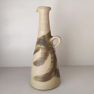 Op de afbeelding: Een hoge, beige keramische vaas met een smalle hals en een klein handvat. De vaas heeft bruine, abstracte penseelstreken. De vaas is ongeveer 30 cm hoog en heeft een getextureerd oppervlak.