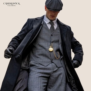 May include: A charcoal grey wool overcoat worn over a grey herringbone three-piece suit, a white collared shirt, a dark patterned tie, and a flat cap. A gold pocket watch with a chain is attached to the vest. Black leather gloves are worn.