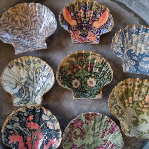 Puede incluir: Conjunto de platos decorativos con forma de concha marina, adornados con intrincados diseños florales y botánicos. Cada concha presenta un diseño único en varios colores, incluyendo rojo, verde, azul y dorado. Los bordes están ribeteados en dorado. Ideal para aperitivos.