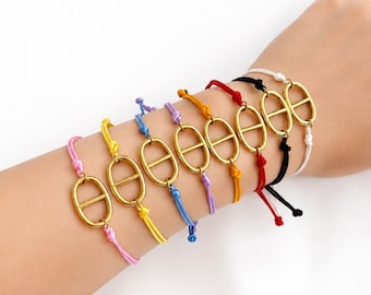 May include: A collection of eight bracelets, each featuring a gold-toned metal oval charm with a horizontal bar across the center. The charms are attached to thin, adjustable cords in pink, yellow, blue, purple, orange, red, black, and white.