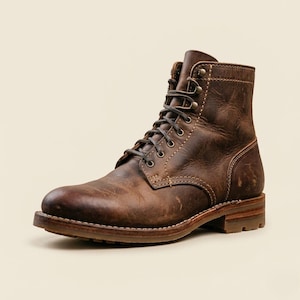 May include: A brown leather lace-up boot featuring a distressed finish, a rounded toe, and a stacked heel. The boot includes dark metal eyelets and speed hooks for the laces, with visible light-colored stitching along the seams and a lugged sole.