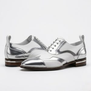 Könnte beinhalten: Ein Paar weiß-silberne Oxford-Schuhe. Die Schuhe haben ein zweifarbiges Design mit weißem Leder und metallisch-silbernen Einsätzen. Die Sohlen sind braun mit einem silbernen Streifen. Mit Zuglasche an der Ferse.