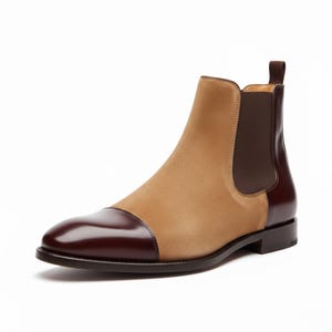 Könnte beinhalten: Zweifarbiger Chelsea-Stiefel mit Obermaterial aus beigefarbenem Wildleder und Zehenkappe sowie Absatz aus dunkelbraunem Leder. Der Stiefel hat eine Zuglasche und ein schlankes, modernes Design. Die Sohle ist dunkelbraun.