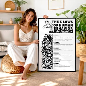 May include: A framed white poster with black text and illustrations titled The 5 Laws of Human Behavior On Stupidity. The design features a cartoon character with a magnifying glass and a dense abstract pattern of black figures below text.