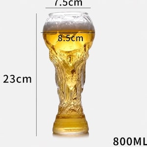 May include: A clear glass beer mug shaped like a trophy, filled with golden beer and white foam. The glass has a height of 23 cm, a top diameter of 7.5 cm, a middle diameter of 8.5 cm, and a total liquid capacity of 800 ml as indicated by text.