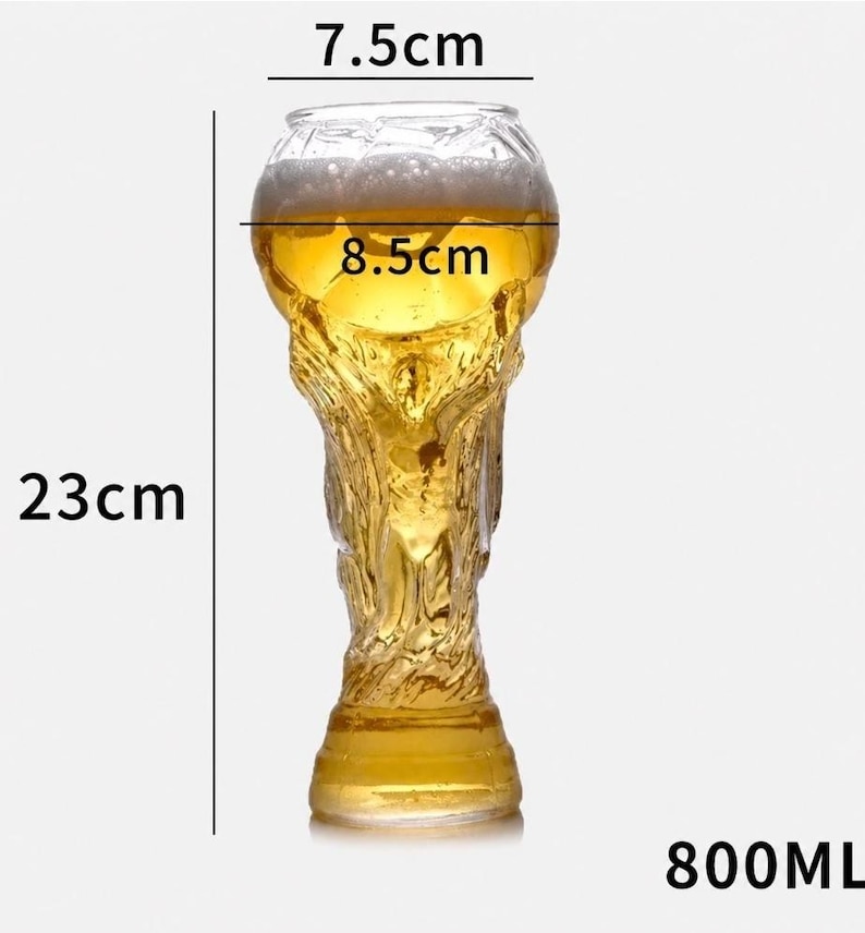 May include: A clear glass beer mug shaped like a trophy, filled with golden beer and white foam. The glass has a height of 23 cm, a top diameter of 7.5 cm, a middle diameter of 8.5 cm, and a total liquid capacity of 800 ml as indicated by text.