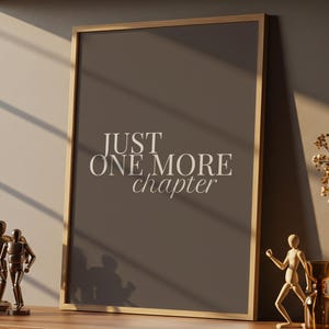 May include: A framed print with the text "JUST ONE MORE chapter" on a wooden cabinet. Decorative items include a vase with dried flowers, sculptures, and books. The scene is illuminated by sunlight.