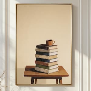 Puede incluir: Impresión enmarcada que muestra una pila de libros sobre una pequeña mesa de madera. Una pequeña taza marrón está encima de los libros. El fondo es de color beige liso y el marco es dorado.