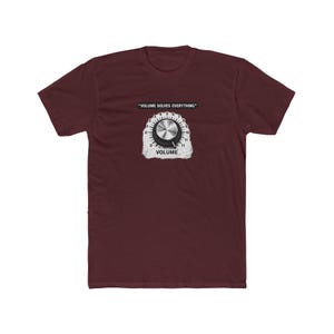 May include: Maroon t-shirt featuring a graphic of a volume knob with the text "VOLUME SOLVES EVERYTHING" above it and "VOLUME" below. The volume knob graphic is silver and black, with a white background.