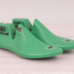 Puede incluir: Un par de hormas de zapatos de color verde brillante. Las hormas tienen una punta redondeada y un talón. La horma izquierda tiene el texto "(E-Z) 25 MAR 2012" y la derecha el número "43".