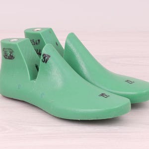 Puede incluir: Se muestran dos hormas de zapatos verdes, utilizadas en la fabricación de calzado. Las hormas están hechas de un material sólido con un acabado liso y ligeramente brillante. El número "37" es visible en una de las hormas.