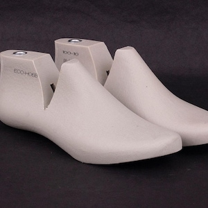 Puede incluir: Un par de hormas de zapato grises claras, diseñadas para dar forma al calzado. Las hormas están hechas de un material sólido y presentan un diseño liso y curvado. El texto "ECO-H066" y "100-10" está impreso en la parte superior.