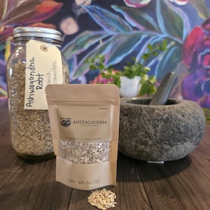 May include: An image featuring ashwagandha root in various forms. A glass jar and a kraft paper bag display the root, with text labels. A stone mortar and pestle are also present, suggesting preparation. The background has a floral design.