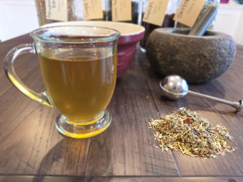 K&ouml;nnte beinhalten: Eine wei&szlig;e Keramik-Tasse mit schwarzem Henkel und dem Text "But First, Coffee" in fetter, schwarzer Schrift. Die Tasse steht vor einem neutralen Hintergrund, der ihr schlichtes Design hervorhebt.