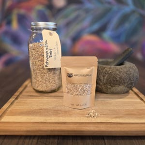 May include: A clear glass jar and a small kraft paper bag filled with ashwagandha root. The jar has a metal lid and a tag that reads "Ashwagandha Root". A stone mortar and pestle are also present on a wooden cutting board.