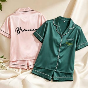 Peut inclure: Deux ensembles de pyjamas en satin. L'un est rose avec "Brianna" brodé au dos. L'autre est vert émeraude avec "Kayla" brodé sur la poche. Les deux ensembles ont une bordure blanche.