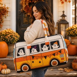 May include: A quilted duffel bag featuring a graphic of a vintage van in orange, yellow, and white. The van design includes ghosts in the windows, a pumpkin wheel, and black bunting. The bag has striped handles and a cream-colored quilted texture.