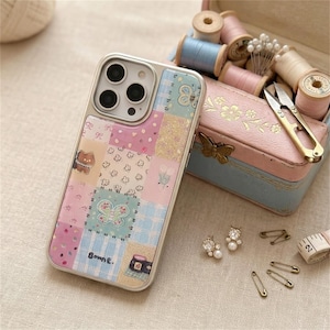May include: A patchwork-style phone case with a silver frame. The case features a mix of pastel pink, blue, and yellow squares with butterfly and floral designs. The case has the text "Bonne E." on the bottom.